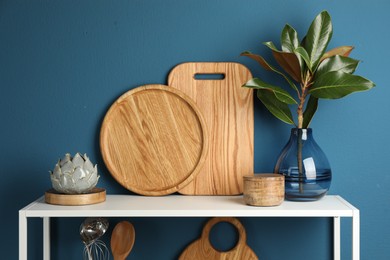 Photo of Wooden cutting boards, branch with green leaves and decor on shelving unit near blue wall