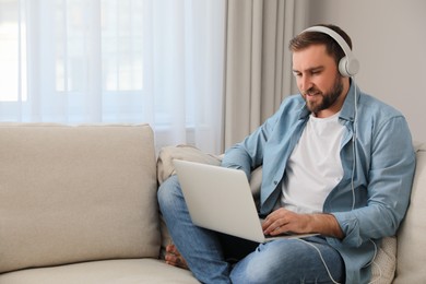 Man with laptop and headphones sitting on sofa at home