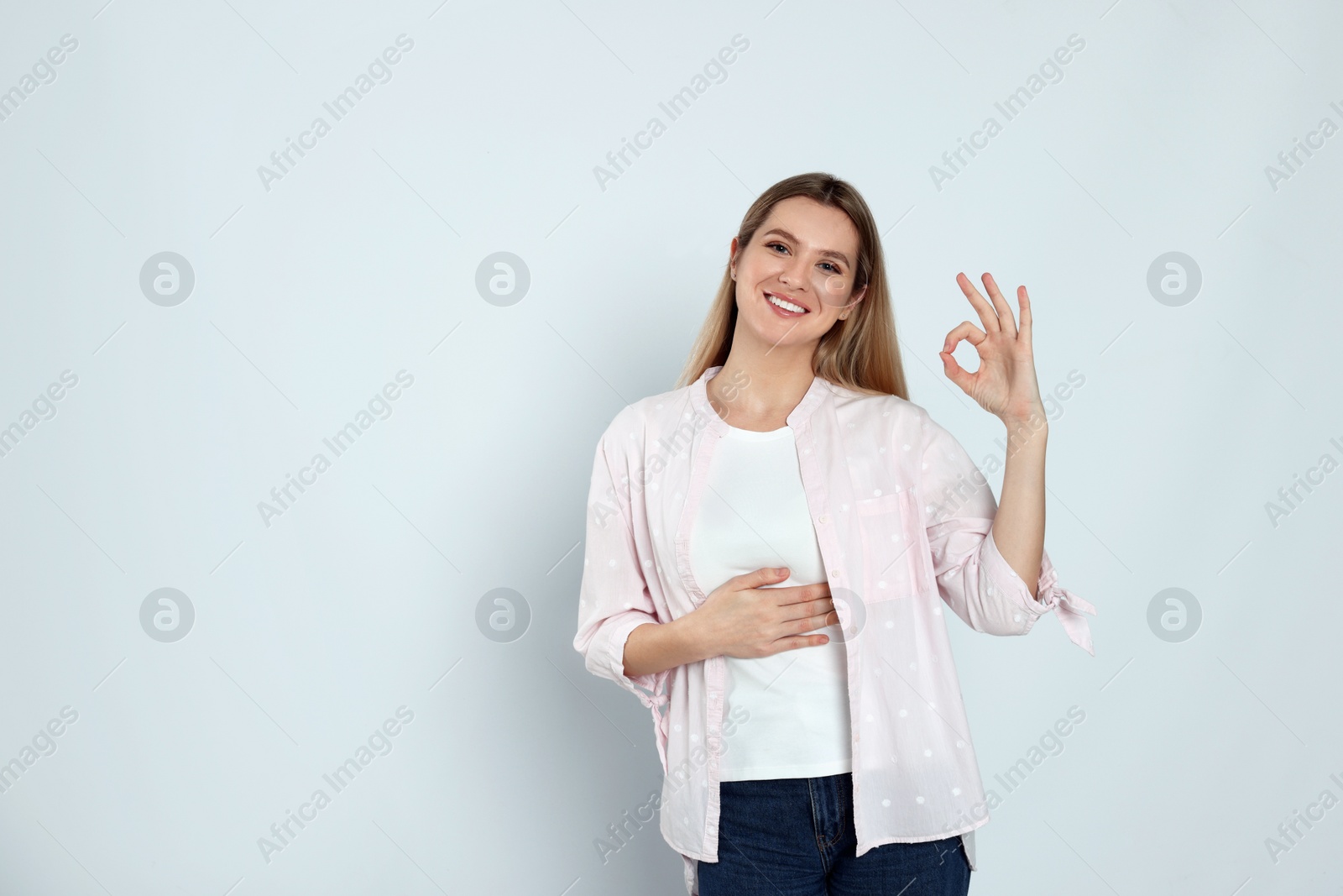 Photo of Happy woman touching her belly and showing okay gesture on light background, space for text. Concept of healthy stomach