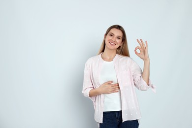 Happy woman touching her belly and showing okay gesture on light background, space for text. Concept of healthy stomach