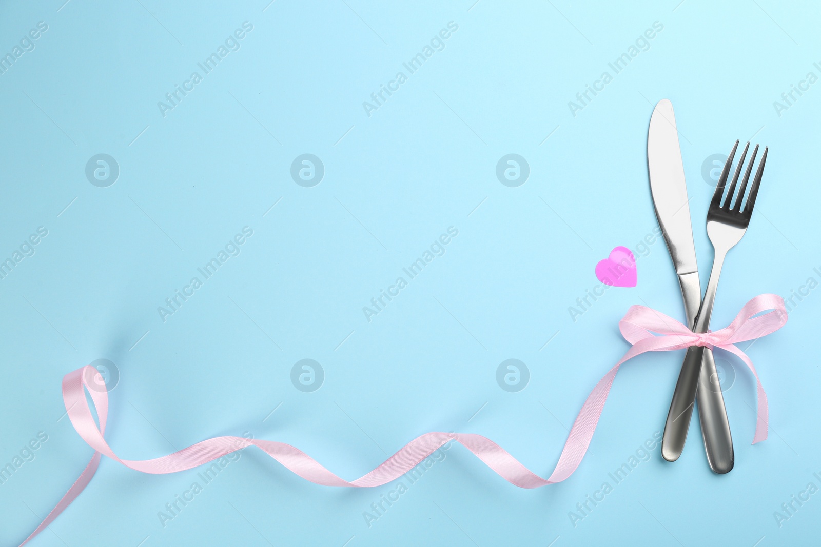 Photo of Beautiful cutlery set, heart and pink bow on light blue background, flat lay with space for text. Valentine's Day dinner