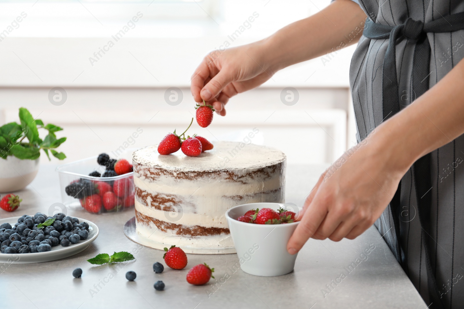 Photo of Woman decorating delicious cake with fresh berries at table. Homemade pastry