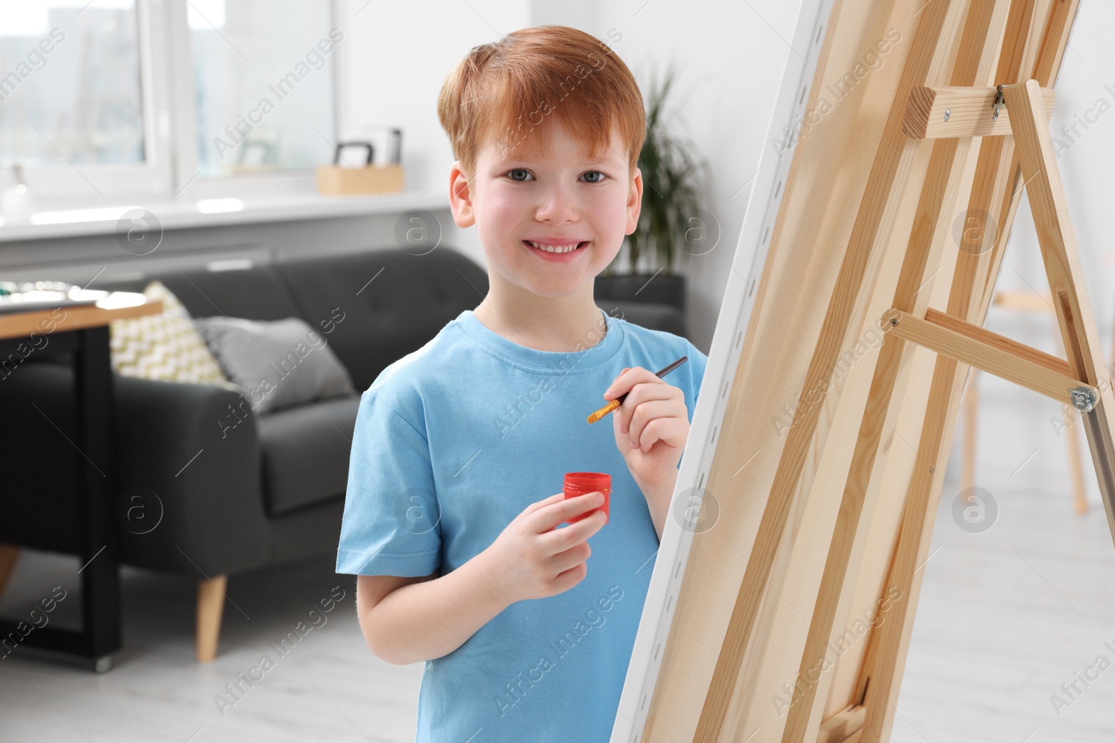 Photo of Happy little boy painting in studio. Using easel to hold canvas