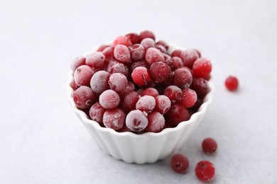 Frozen red cranberries in bowl on light table, closeup