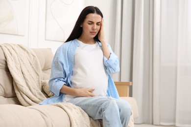 Pregnant woman suffering from headache on sofa at home, space for text