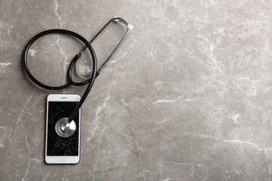 Photo of Modern smartphone with broken display, stethoscope and space for text on table, flat lay. Device repair service
