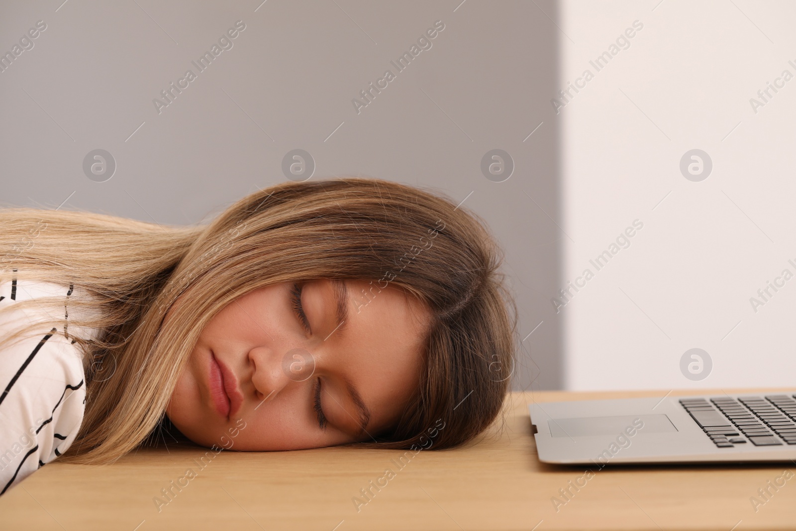 Photo of Young woman sleeping in front of laptop at wooden table indoors