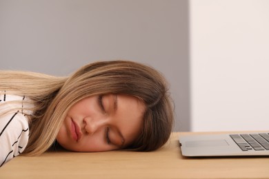 Photo of Young woman sleeping in front of laptop at wooden table indoors
