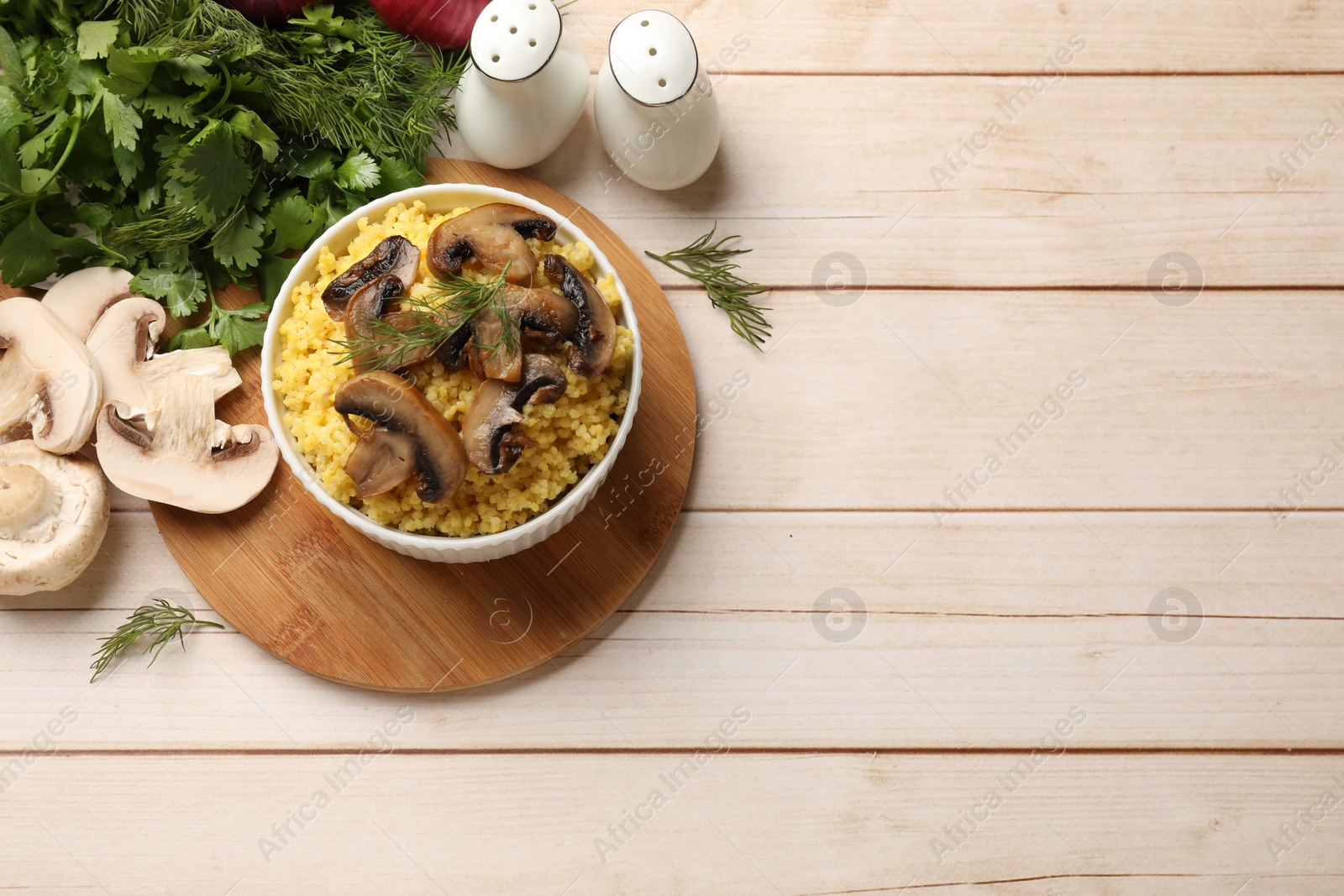 Photo of Tasty millet porridge, mushrooms and dill in bowl on light wooden table, flat lay. Space for text