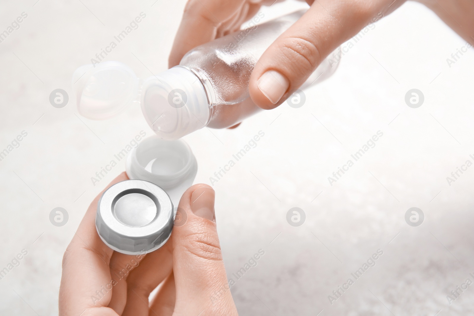 Photo of Woman dripping solution into contact lens case on light background, closeup