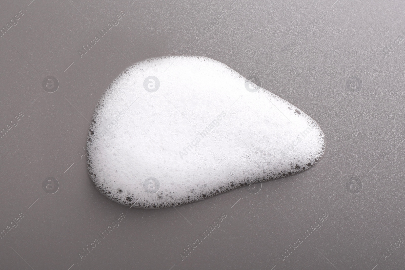 Photo of White foam with bubbles on grey background, above view