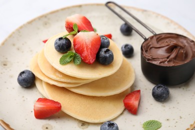 Photo of Delicious pancakes with berries and chocolate spread on plate, closeup