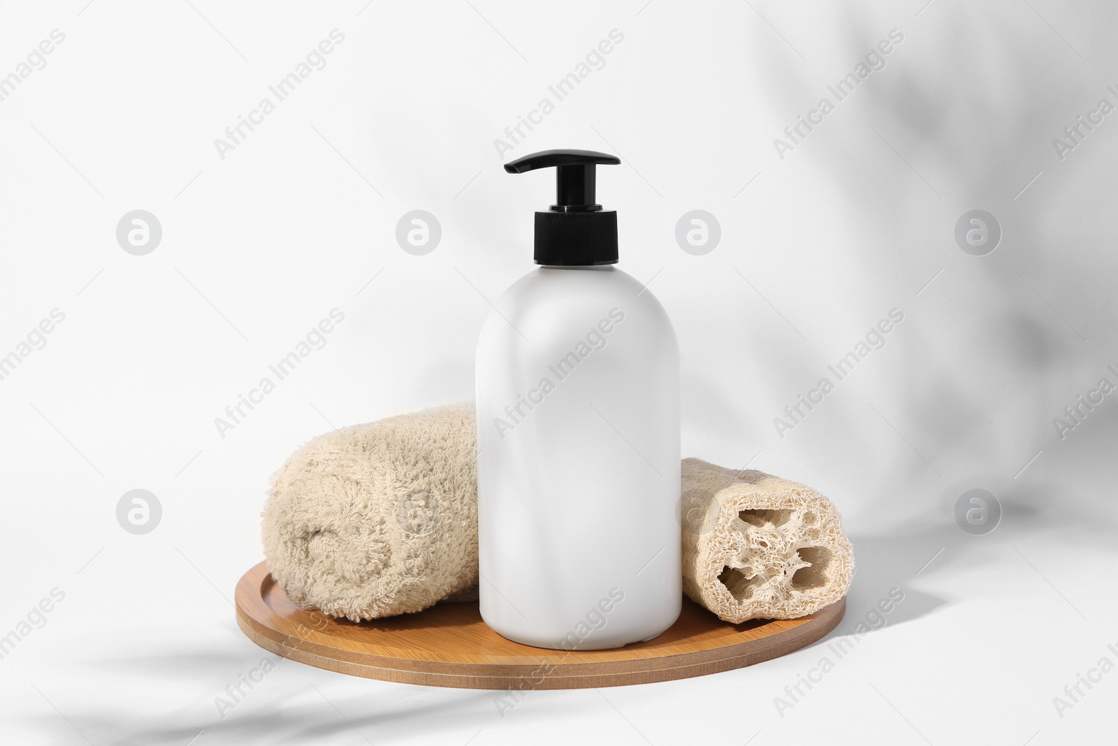 Photo of Bottle with cosmetic product, rolled towel and loofah sponge on white background