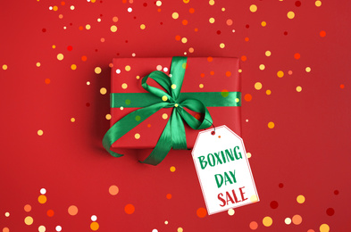 Image of Tag wth text Boxing Day Sale attached to gift on red background, top view