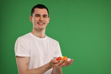 Photo of Easter celebration. Handsome young man holding painted eggs on green background. Space for text