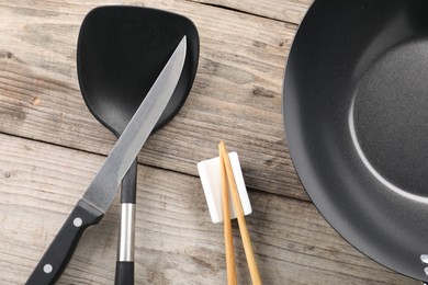 Black metal wok, chopsticks, knife and spatula on wooden table, flat lay