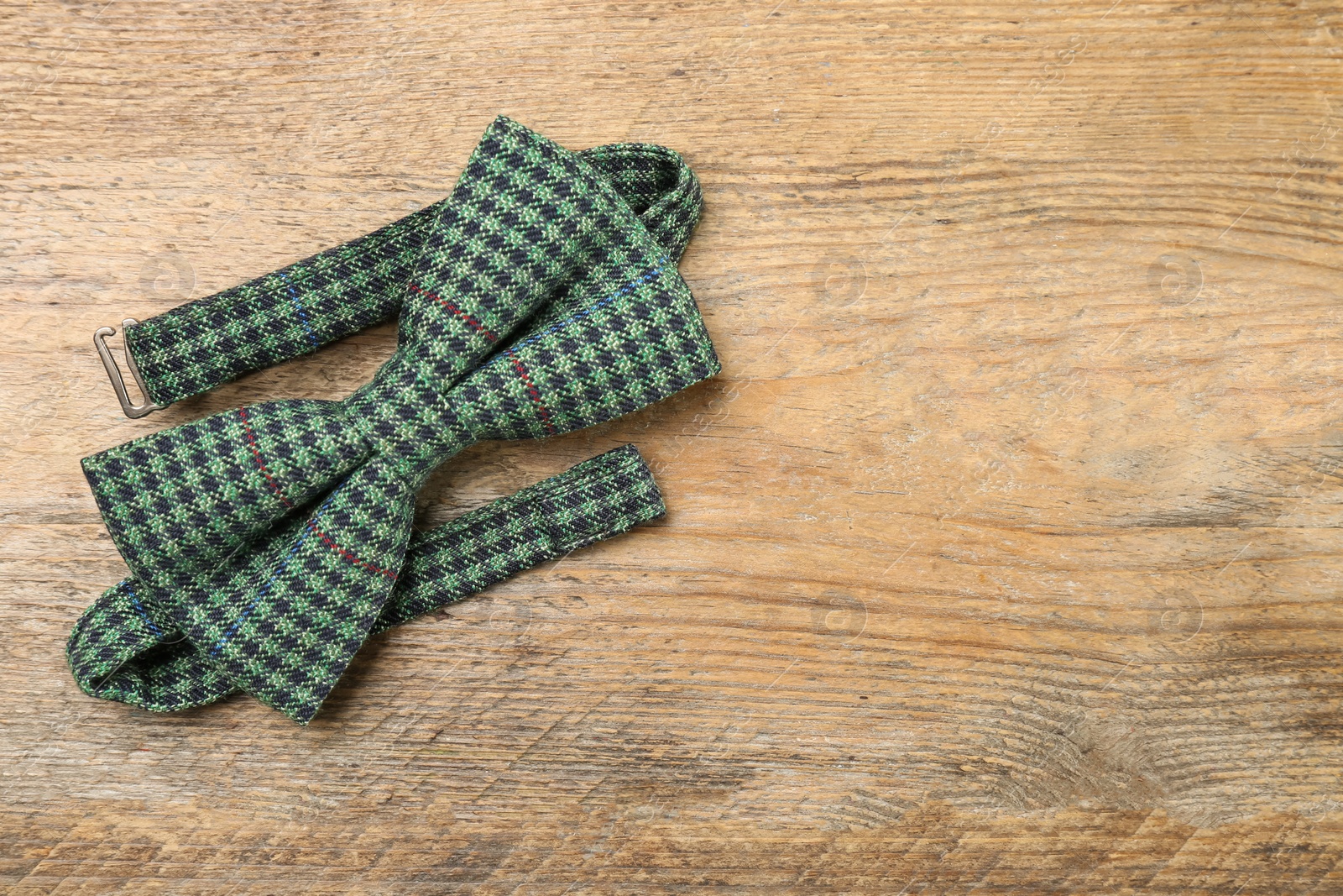 Photo of Stylish checkered bow tie on wooden background, top view. Space for text