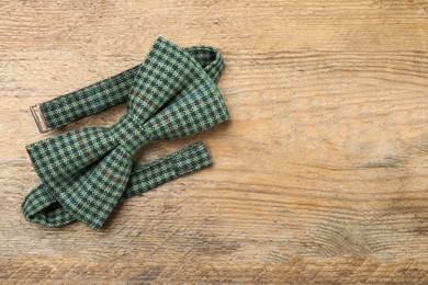 Stylish checkered bow tie on wooden background, top view. Space for text