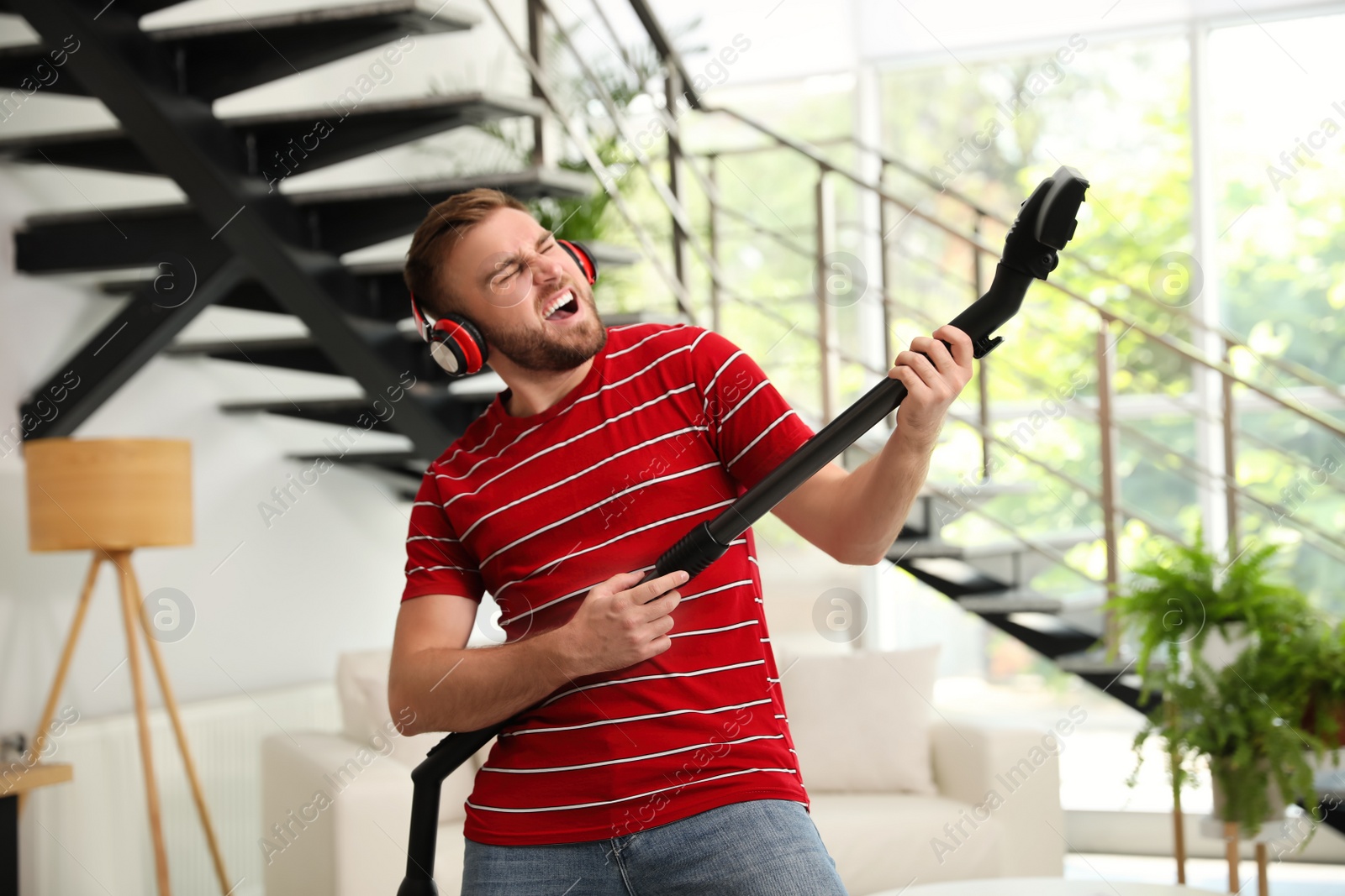 Photo of Young man having fun while vacuuming in living room