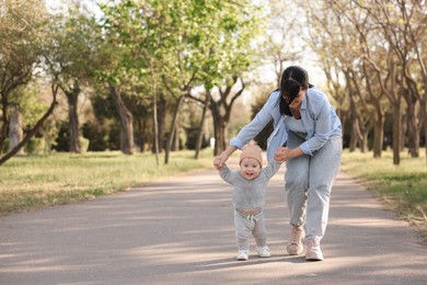 Mother supporting her baby while he learning to walk outdoors. Space for text