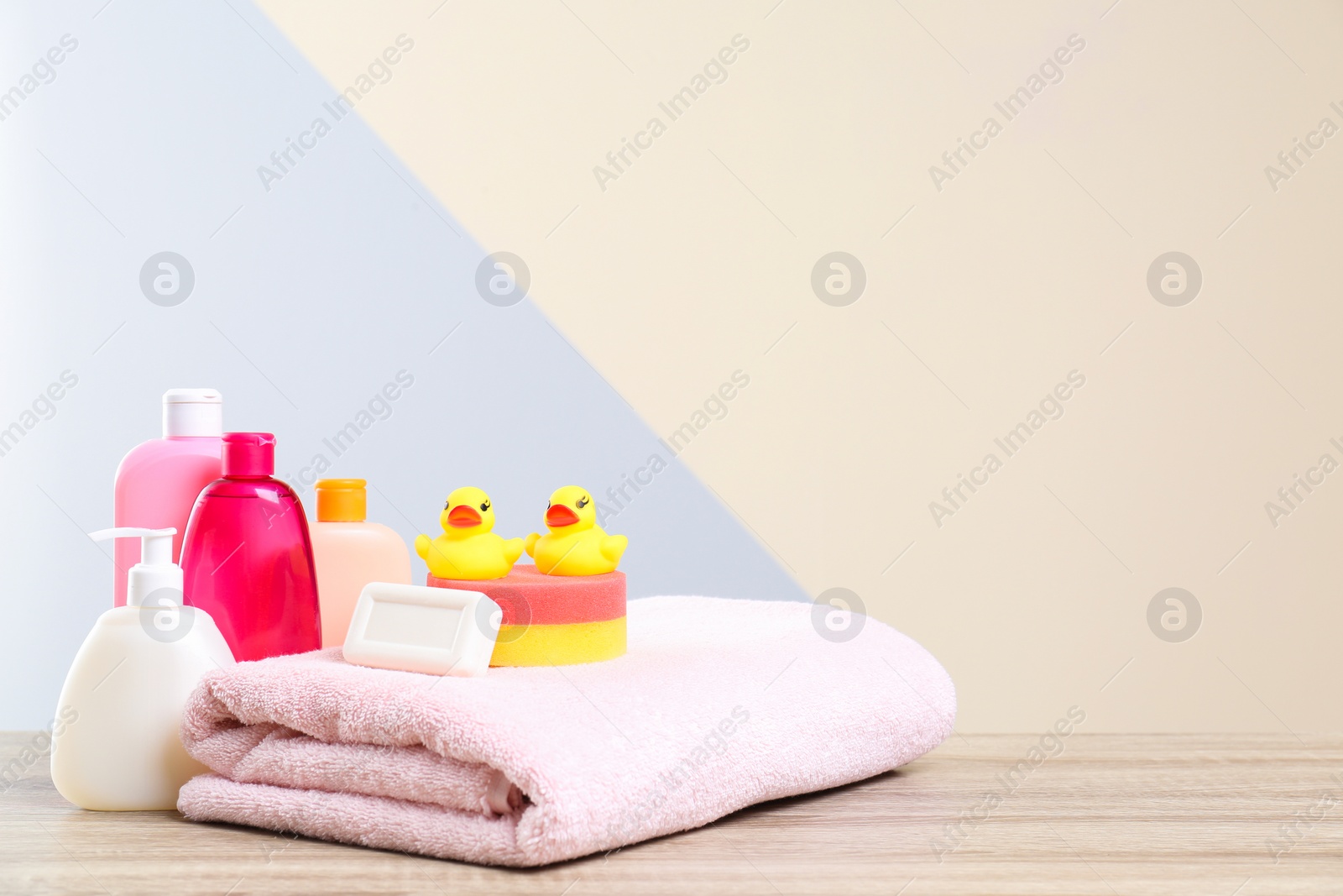 Photo of Baby cosmetic products, toys and towel on table against color background. Space for text