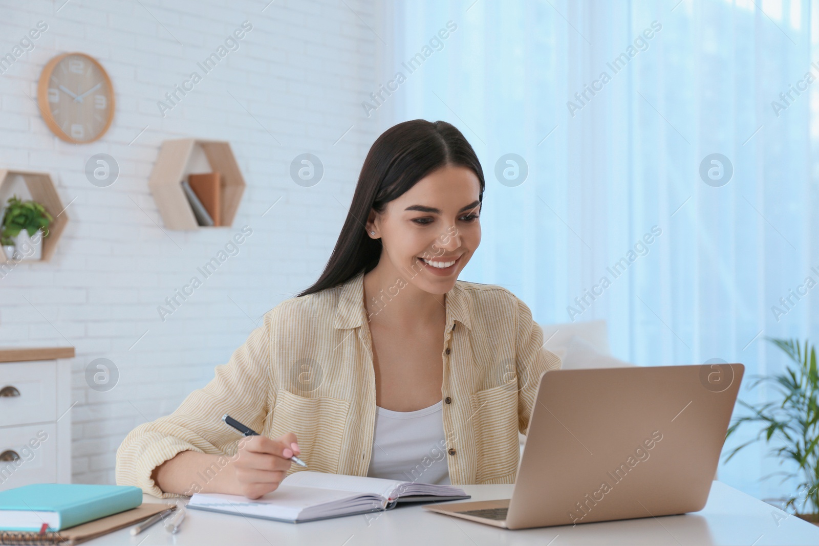 Photo of Young woman taking notes during online webinar at table indoors