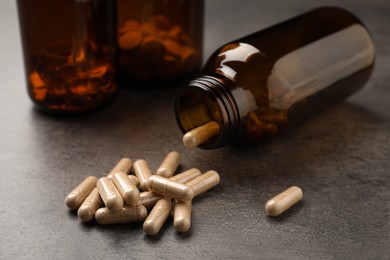 Overturned bottle with dietary supplement capsules on grey table