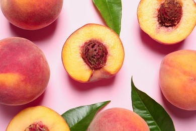 Photo of Cut and whole fresh ripe peaches with green leaves on pink background, flat lay