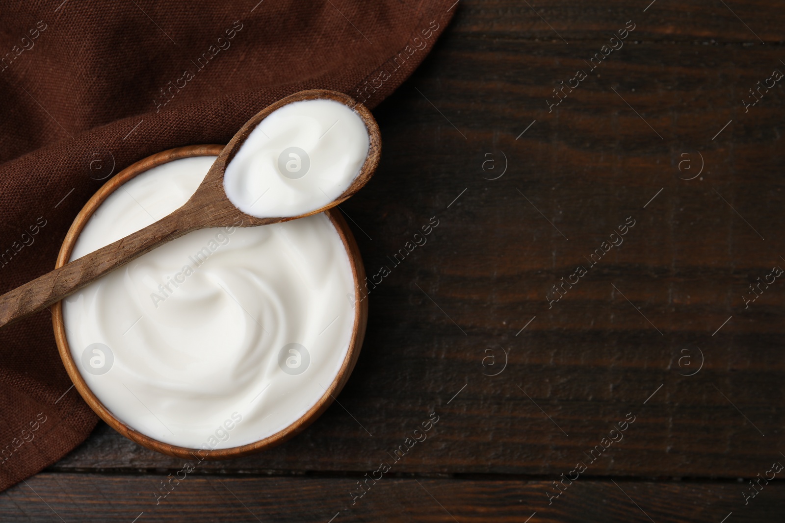 Photo of Delicious natural yogurt in bowl and spoon on wooden table, top view. Space for text