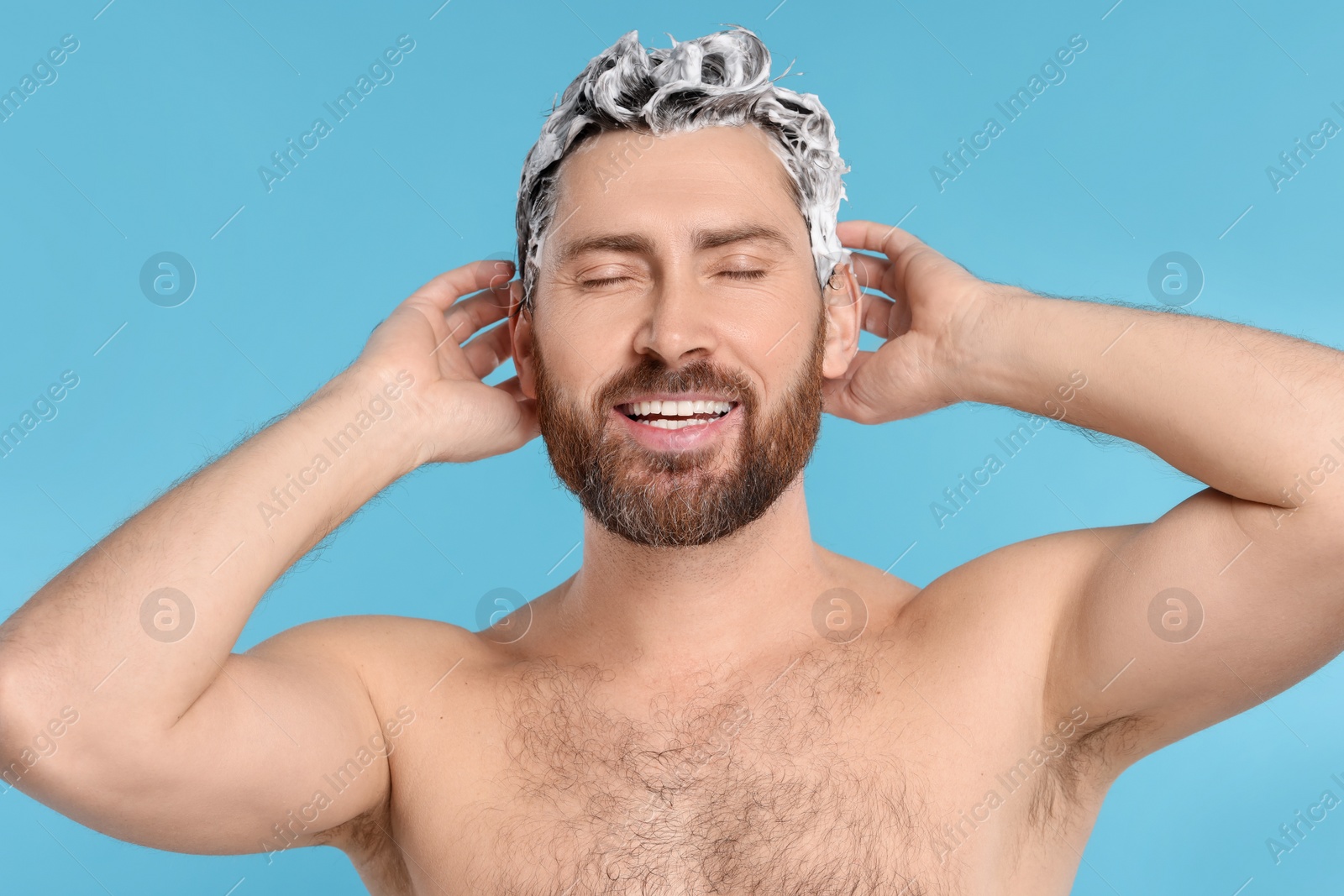 Photo of Happy man washing his hair with shampoo on light blue background