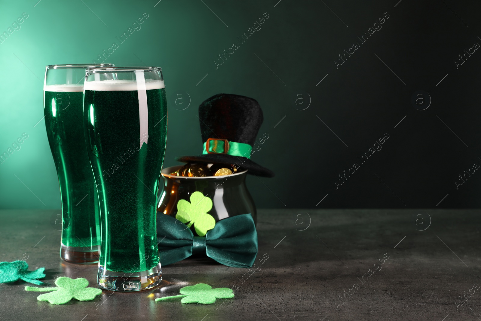 Photo of St. Patrick's day celebration. Green beer, leprechaun hat, pot of gold and decorative clover leaves on grey table. Space for text