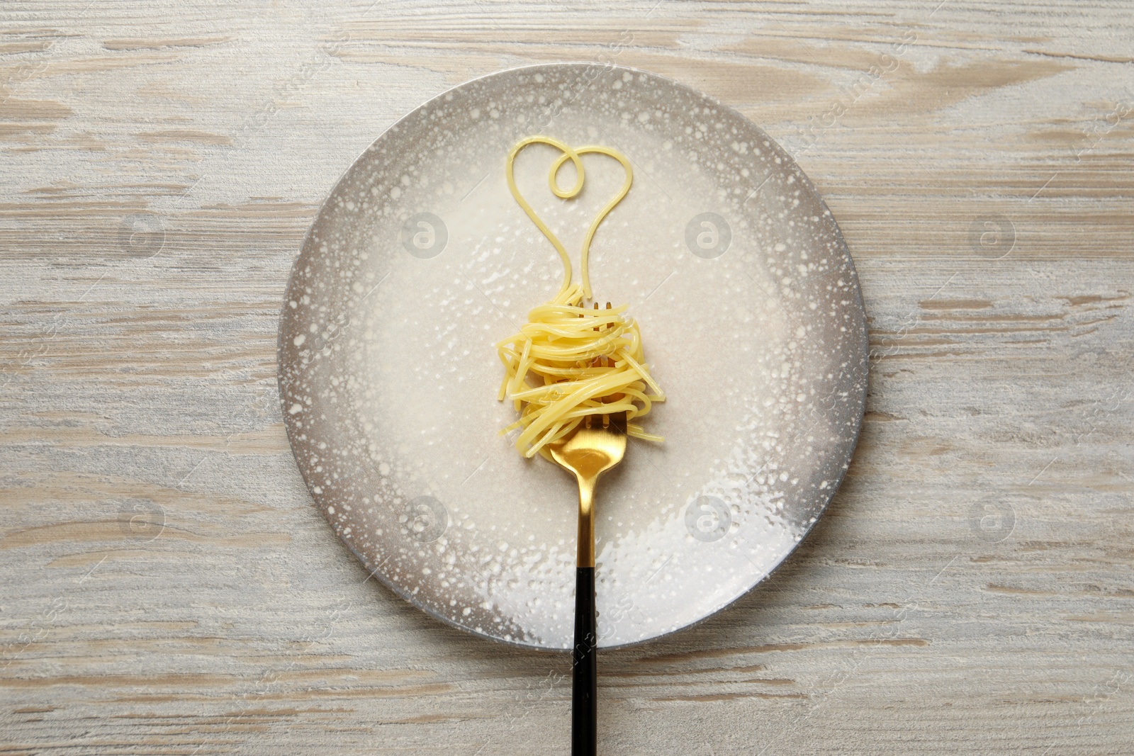 Photo of Heart made with spaghetti and fork on light wooden table, top view