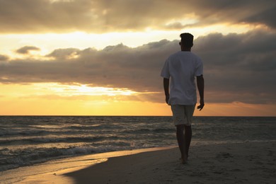 Photo of Man walking on sandy beach during sunset, back view