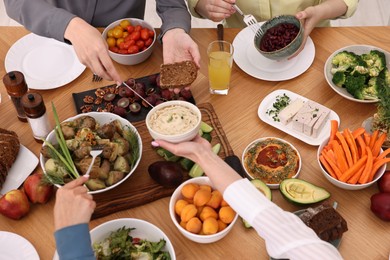 Photo of Friends eating vegetarian food at wooden table indoors, closeup