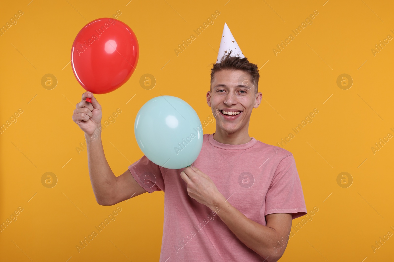 Photo of Happy man in party hat with balloons on orange background