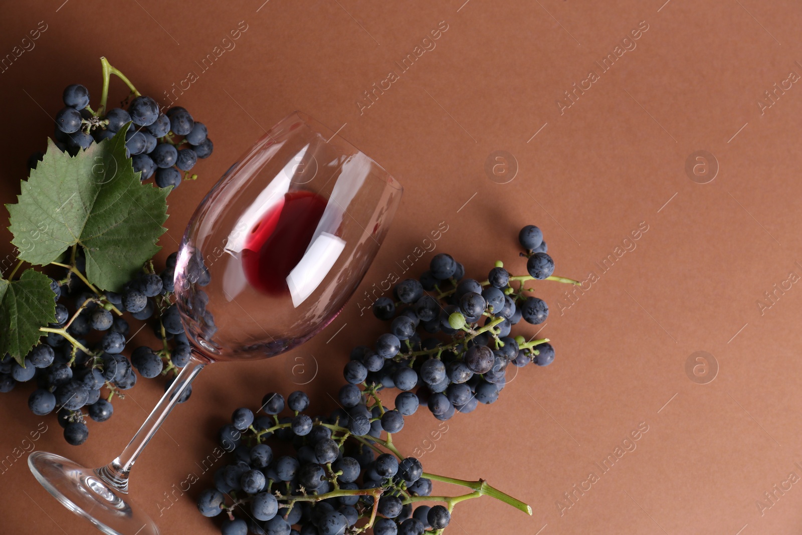 Photo of Overturned glass with red wine and grapes on brown background, flat lay. Space for text