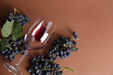 Photo of Overturned glass with red wine and grapes on brown background, flat lay. Space for text