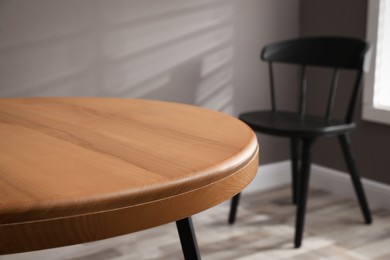 Photo of Round wooden table and black chair in room, closeup