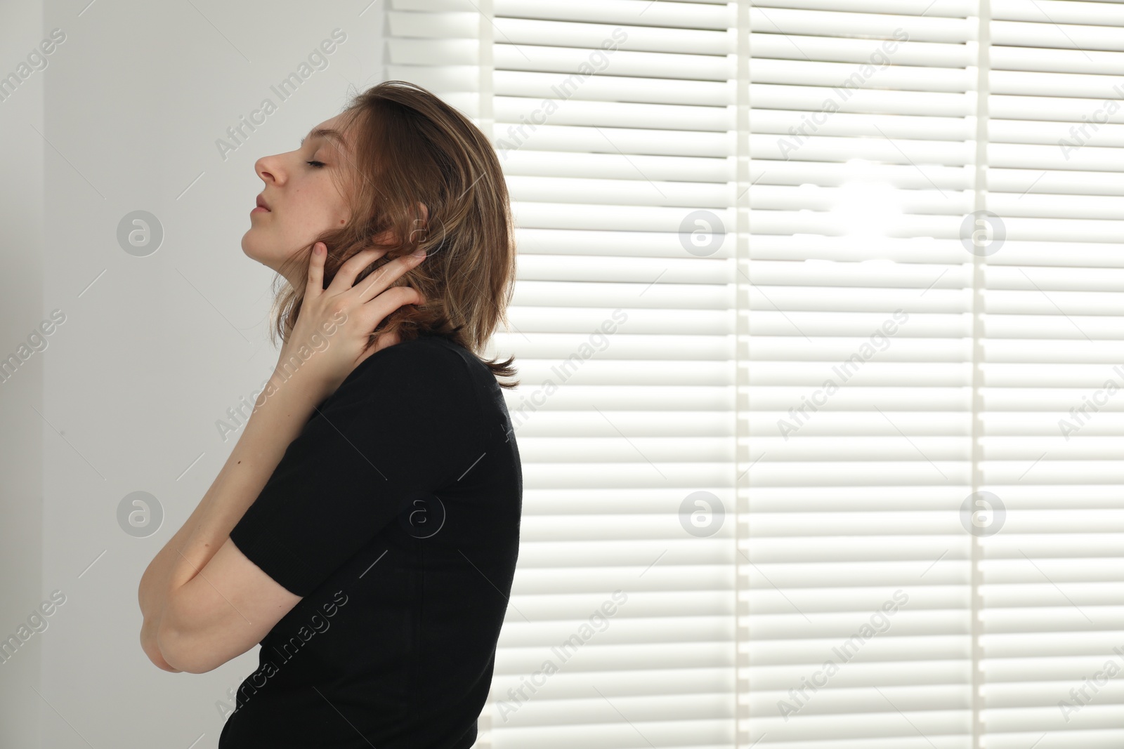 Photo of Sad young woman near closed blinds indoors, space for text