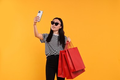Photo of Smiling woman with shopping bags taking selfie on yellow background