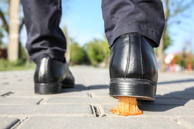 Photo of Man stepping in chewing gum on sidewalk. Concept of stickiness