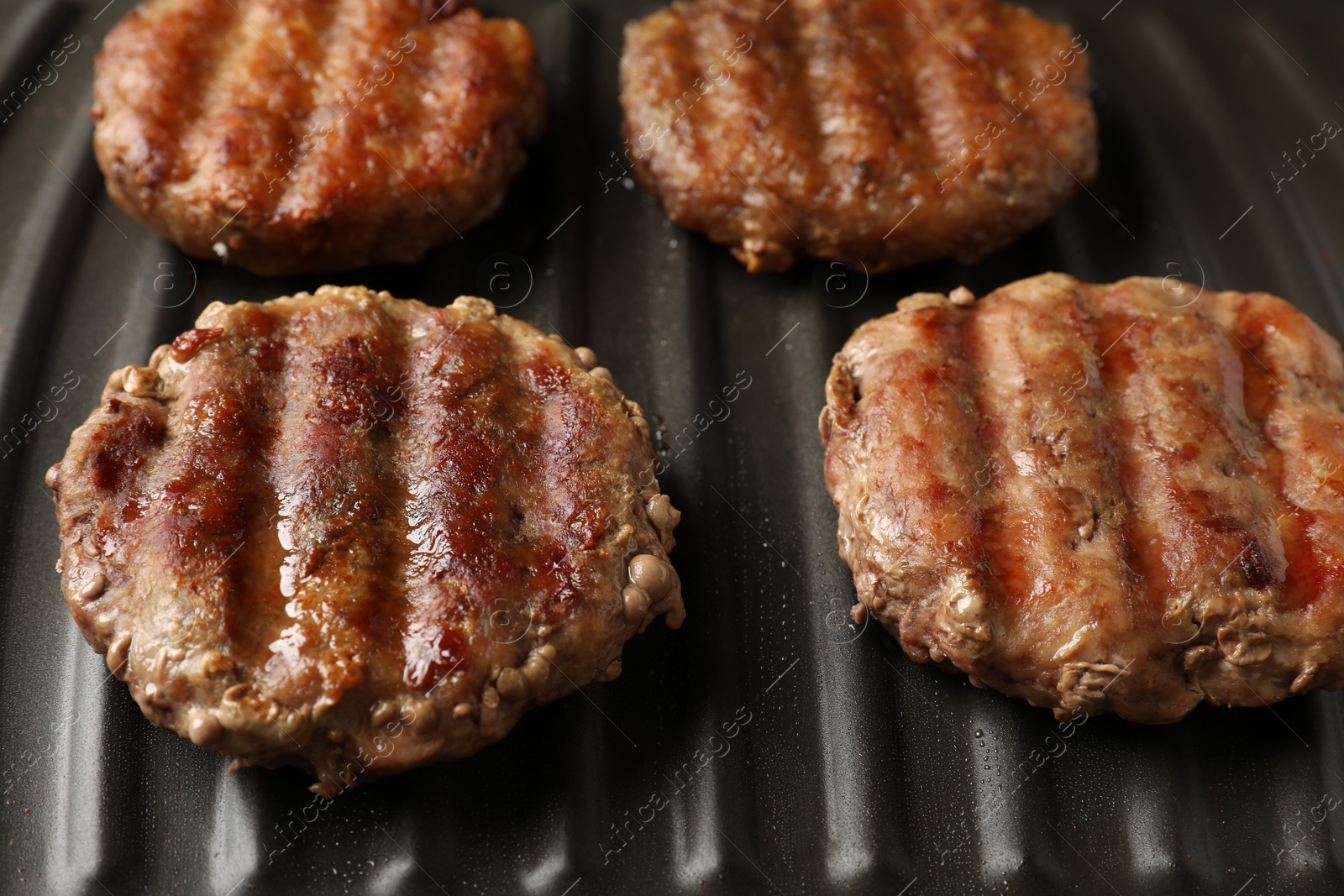 Photo of Delicious hamburger patties cooking on electric grill, closeup