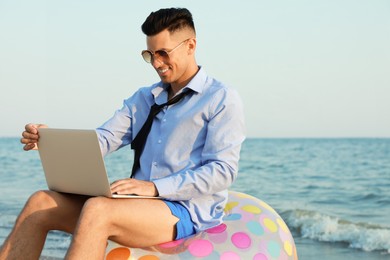 Photo of Happy businessman working with laptop on beach. Business trip
