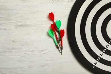 Dart board with color arrows on white wooden background, top view. Space for text