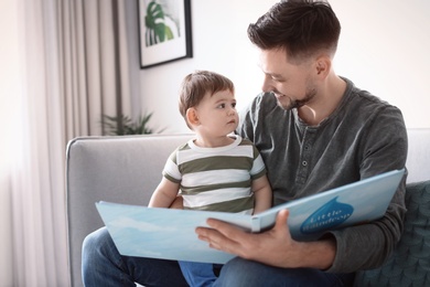 Photo of Dad and his son reading book on sofa at home