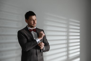 Photo of Man wearing stylish suit and cufflinks near white wall, space for text