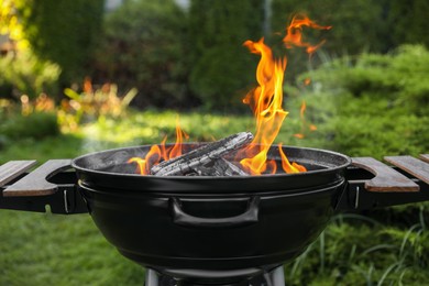 Photo of Portable barbecue grill with fire flames outdoors, closeup
