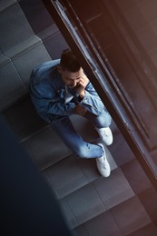 Upset man sitting on stairs indoors, top view. Loneliness concept