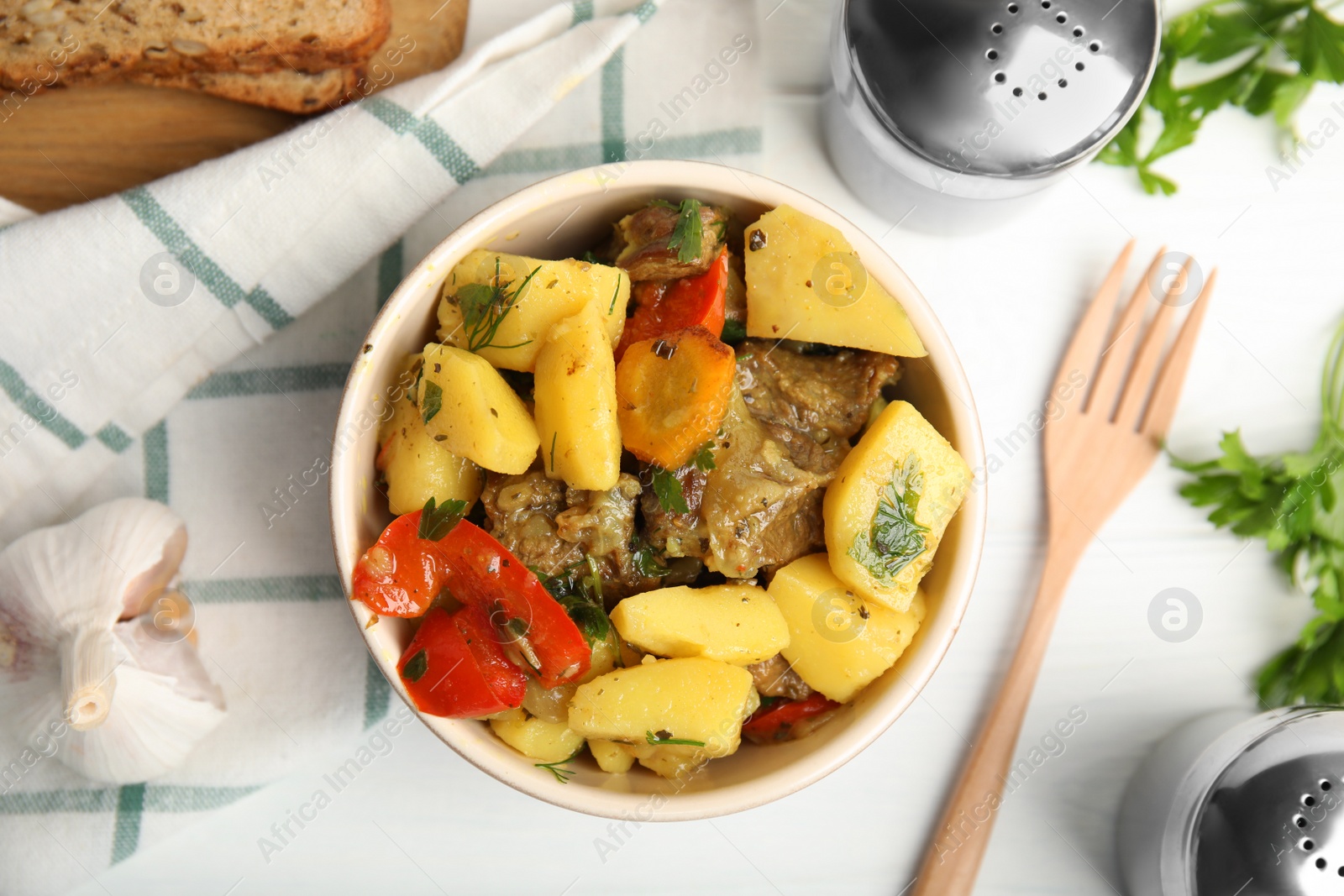 Photo of Tasty cooked dish with potatoes in earthenware served on white wooden table, flat lay