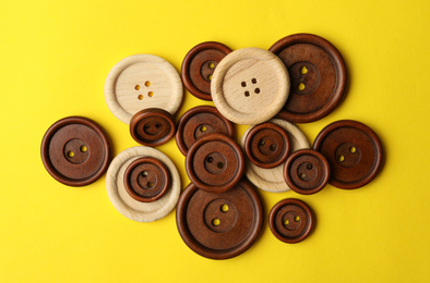 Many colorful sewing buttons on yellow background, flat lay